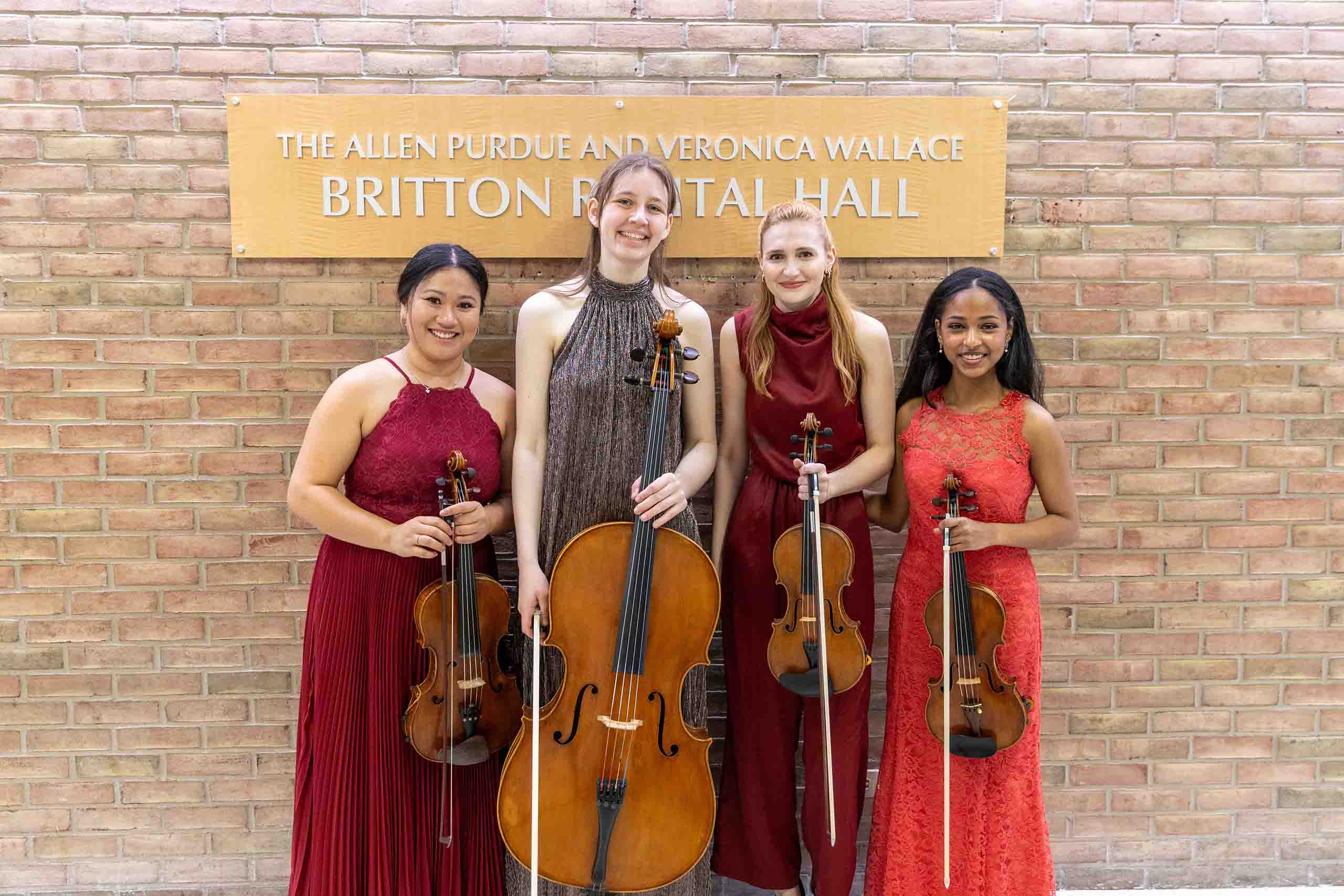 Trio poses standing outside Britton Recital Hall, holding instruments