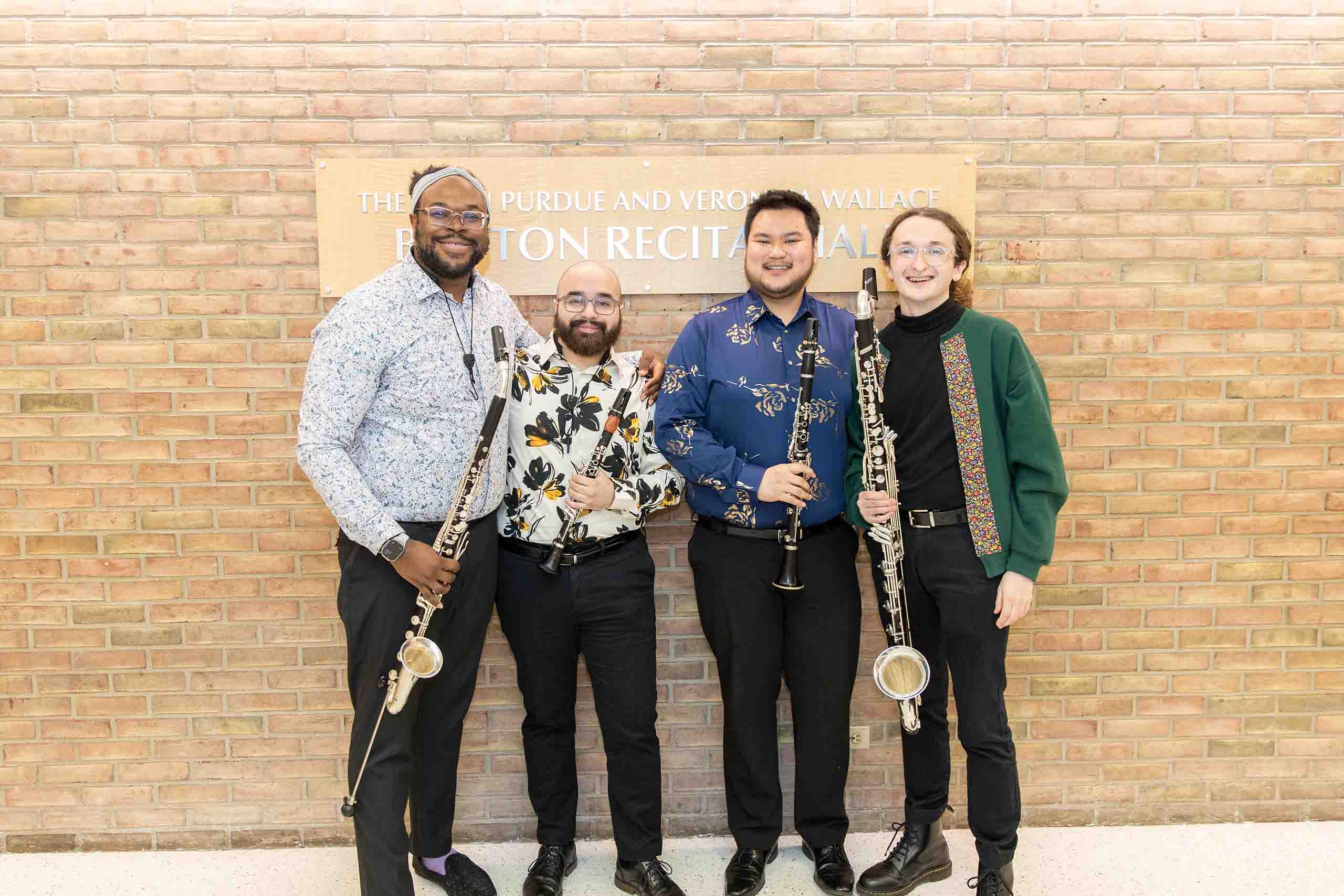 Trio poses standing outside Britton Recital Hall, holding instruments