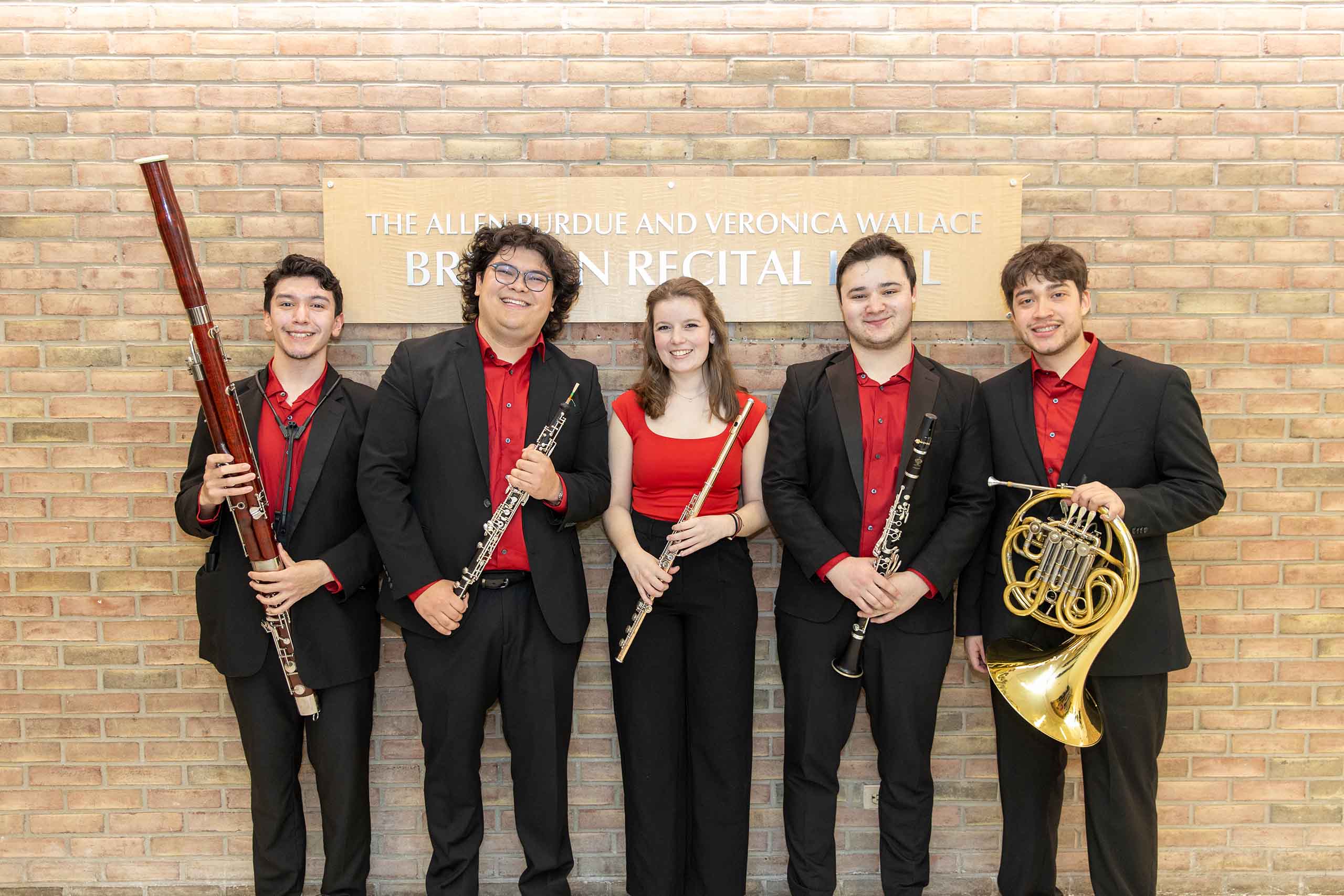 Trio poses standing outside Britton Recital Hall, holding instruments