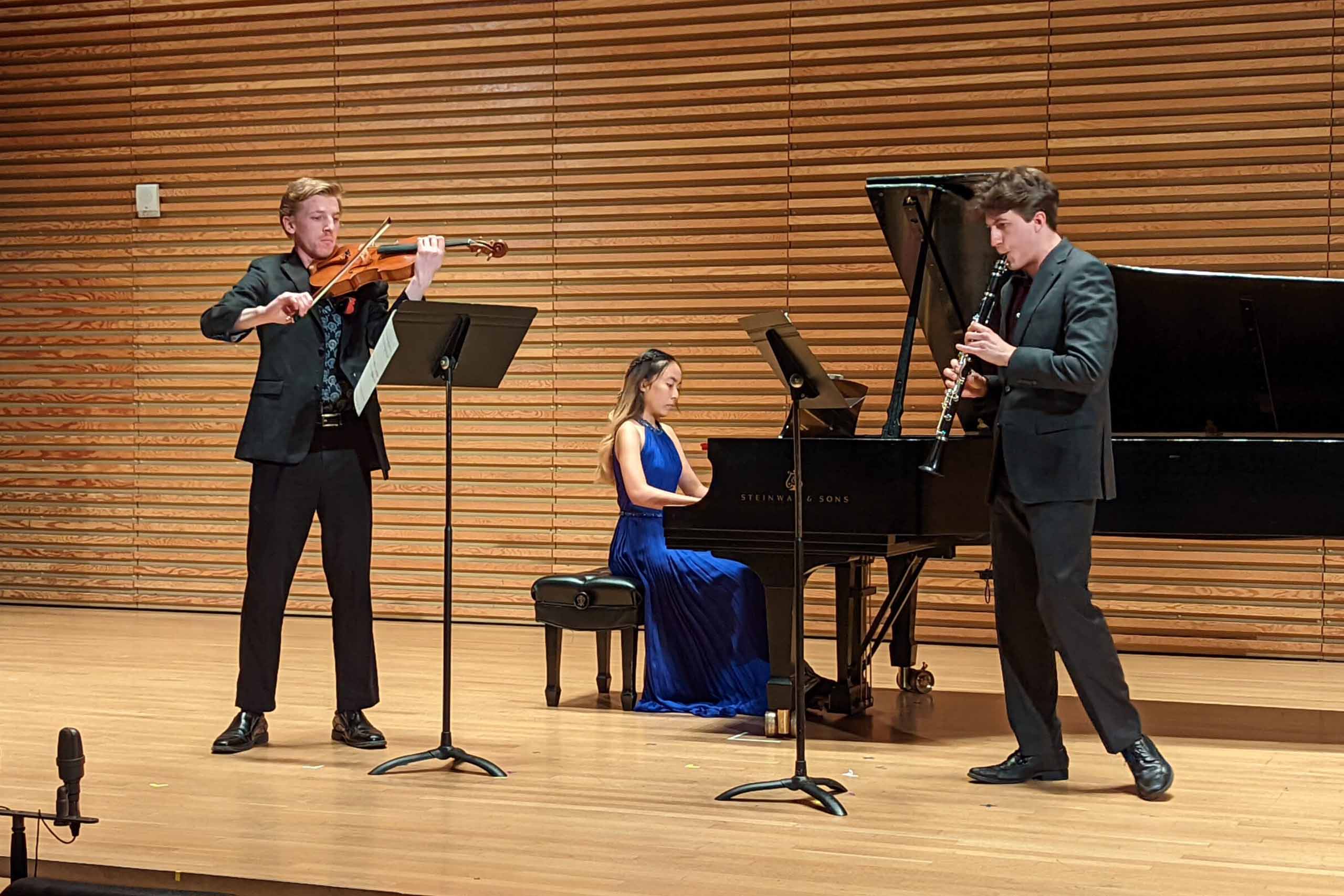 A trio of a violinist, pianist, and oboist performing on the Stamps Auditorium stage.