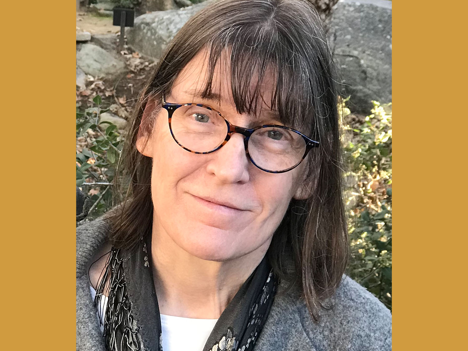 Headshot of Patricia Hall taken outdoors wearing a grey sweater and dark scarf, with gold color background.