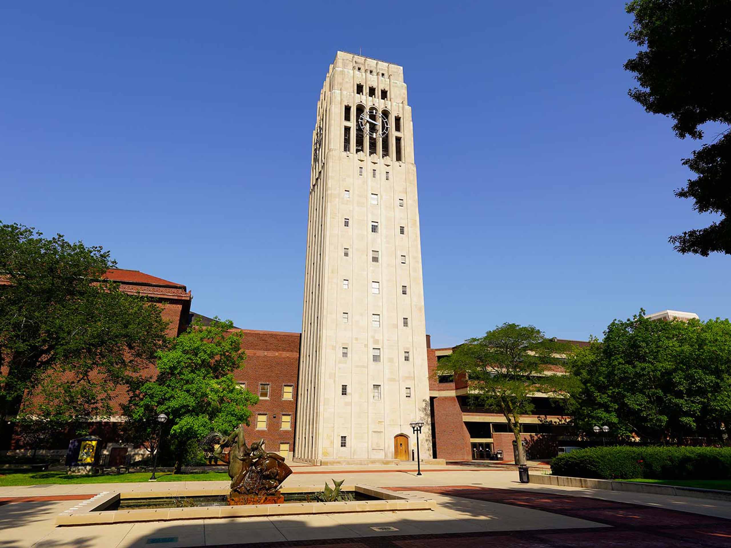 The full Burton Memorial Tower captured on a sunny summer day, with the fountain and Hill Auditorium seen adjacent.