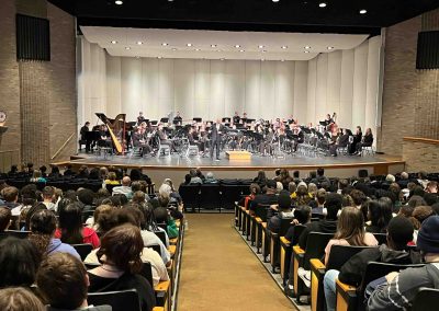 In the Belleville High School auditorium, an audience fills the seats facing the Symphony Band and a speaker on stage.