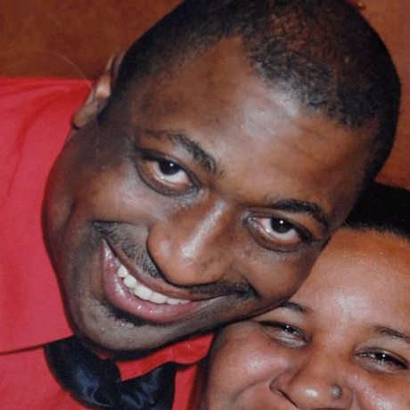 Casual photo of Eric Garner in loving embrace, wearing a red collared shirt and black tie.