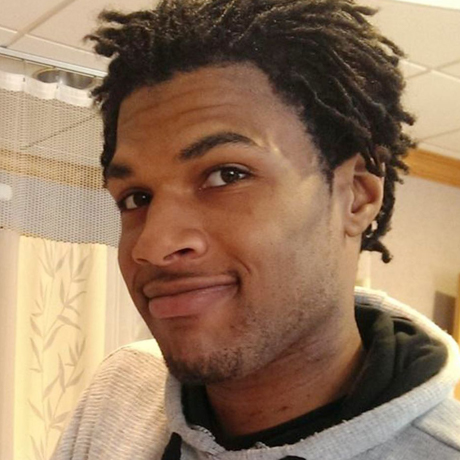 John Crawford poses standing, wearing a grey hoodie.
