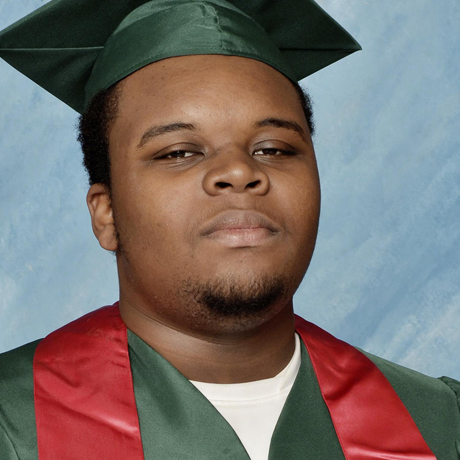 Portrait of Michael Brown wearing green graduation cap and gown.