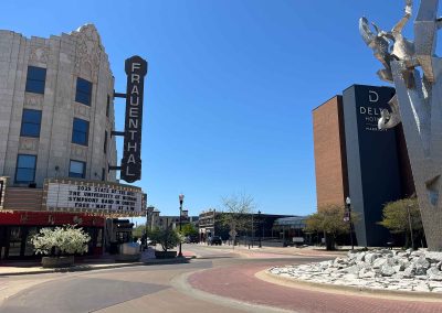 View of a Muskegon city street, with a tall silver sculpture across from the Frauenthal Theater, where the marquee promotes "The University of Michigan Symphony Band in Concert."