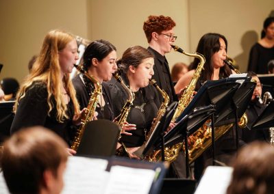 Close-up of a row of five saxophone players standing, attired in concert black, while performing on stage with the Symphony Band.