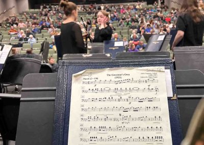 A view of music on a stand as the band prepares to take the stage in a Traverse City auditorium, facing a crowded audience in the house.
