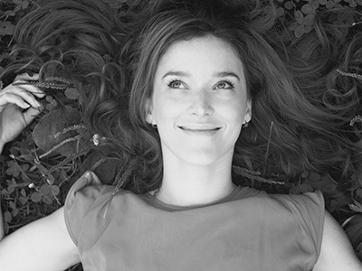 Black and white headshot of Leah O'donnell laying down in the grass, with one arm raised