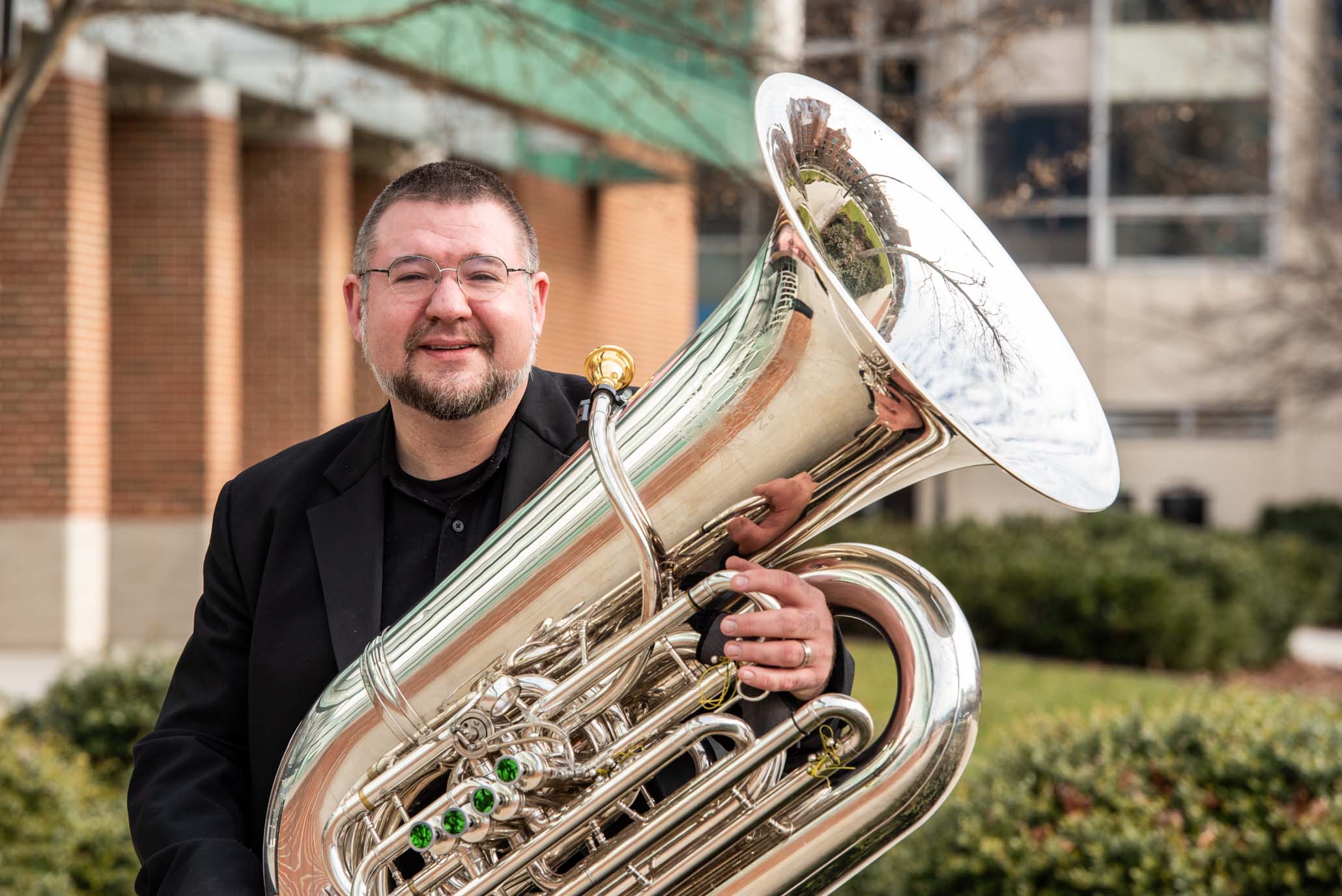 Portrait of Alexander Lapins standing outdoors with his tuba on a campus.
