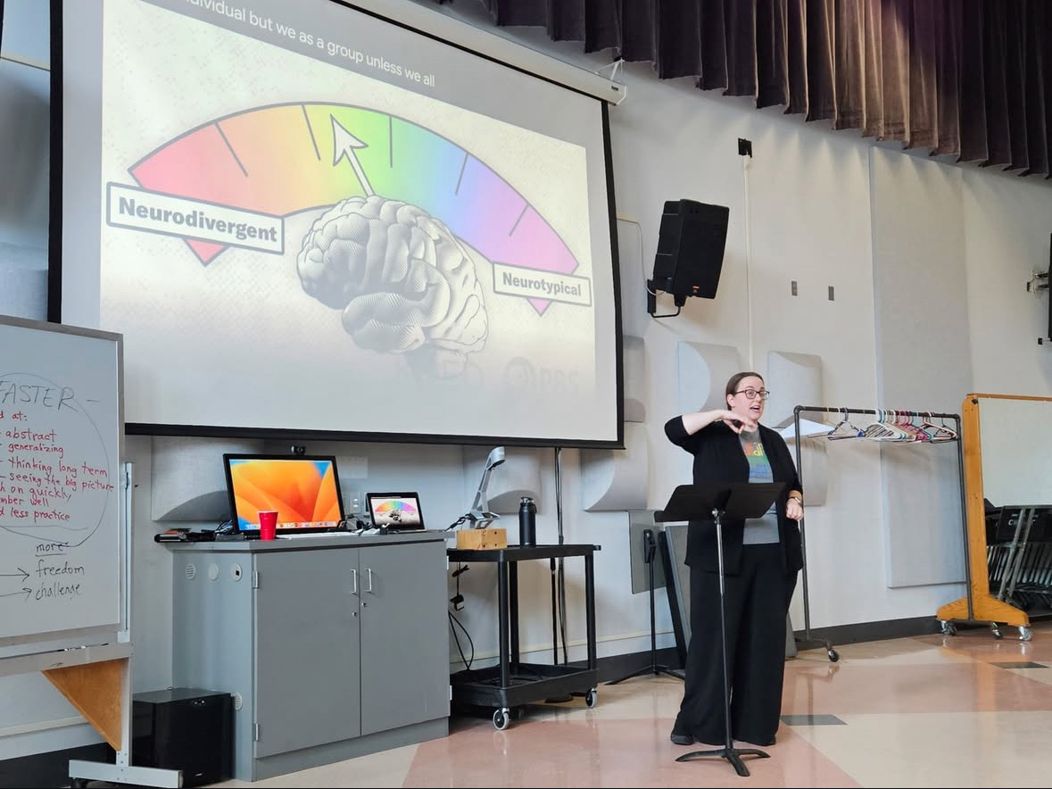 Corinne Galligan keynote lecture at Lawrence University Music Education Symposium Corinne Galligan speaks standing in a classroom space, in front of a large slide projection.
