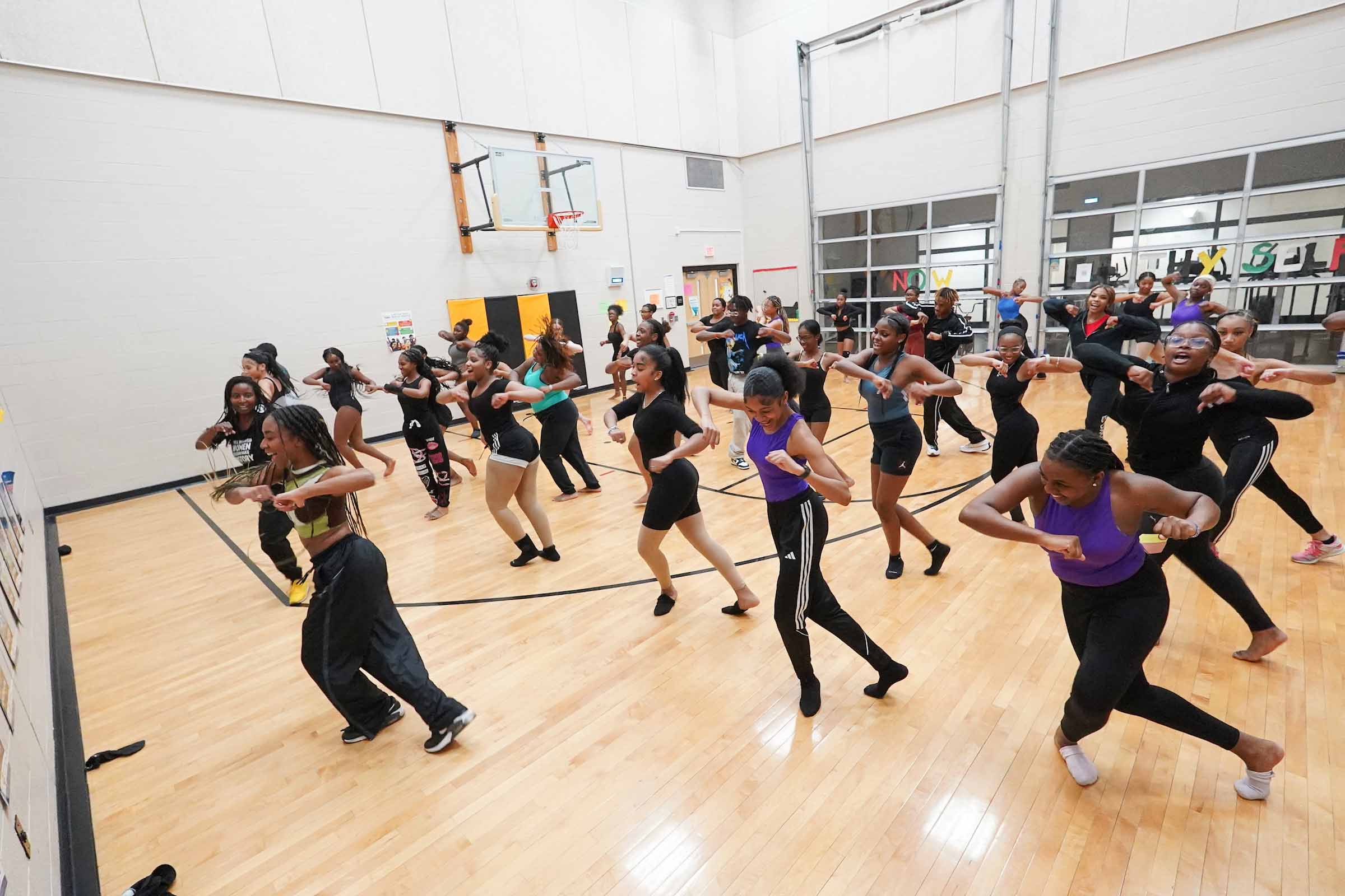 Dance Day Community Collaboration Detroit March 2024-05 Over two dozen young dancers in rehearsal, stepping together with elbows out in a gymnasium space.