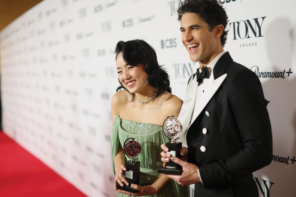 Shen and Criss pose holding their Tony Awards on a red carpet, in formal attire.