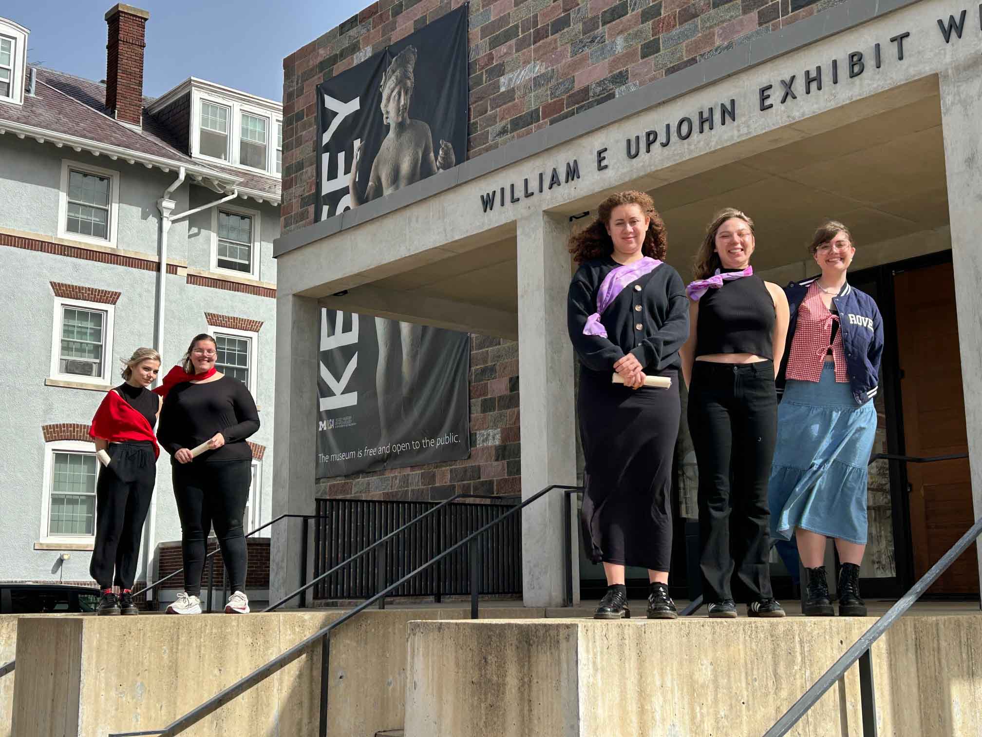 Julius Caesar students at Kelsey Museum of Archaeology Five students pose standing outside the Kelsey Museum on a sunny day; four are attired in all black with a red or purple scarf.
