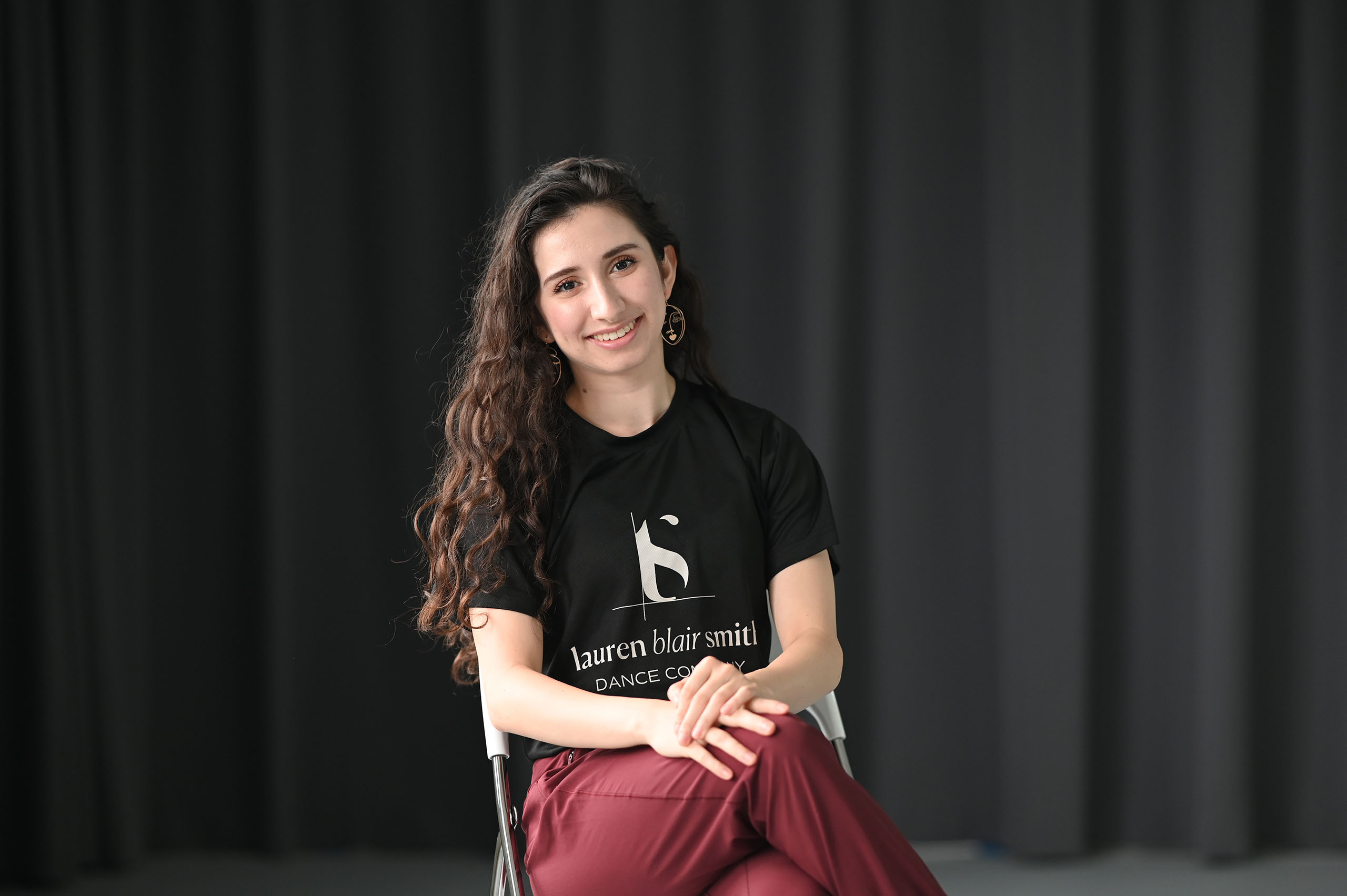 Lauren Blair Smith Photo Lam Photography Lauren Blair Smith poses seated in a studio space with a black curtain in the background.