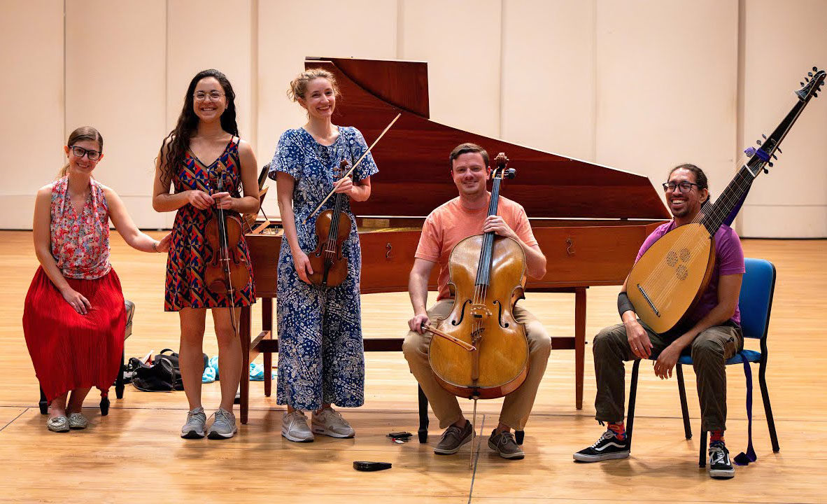 Five musicians pose together with string instruments and a harpsichord.