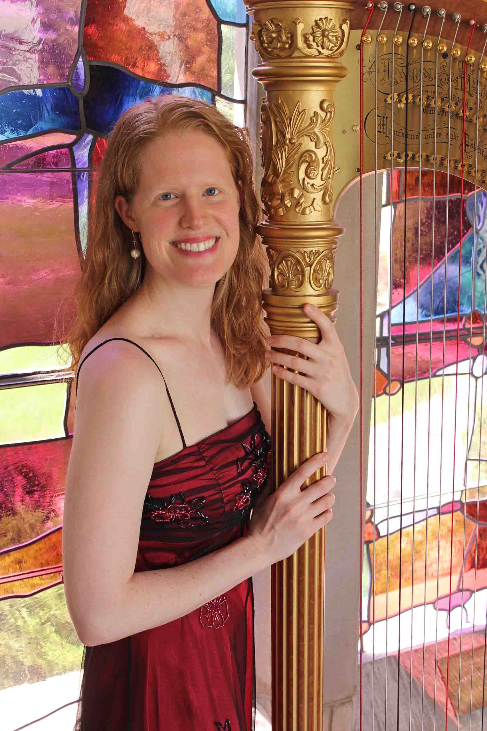 Rachel Brandwein poses next to a carved gold harp, in front of a stained glass window.