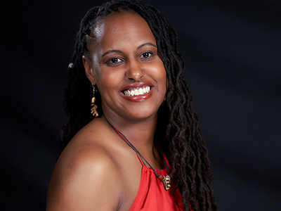 Headshot of Tamara Tucker-Ibarisha against a black background, wearing a red dress and matching beaded necklace and earrings