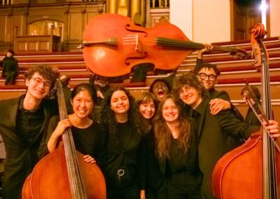 A group of 8 students poses with 3 double basses, attired in concert black.