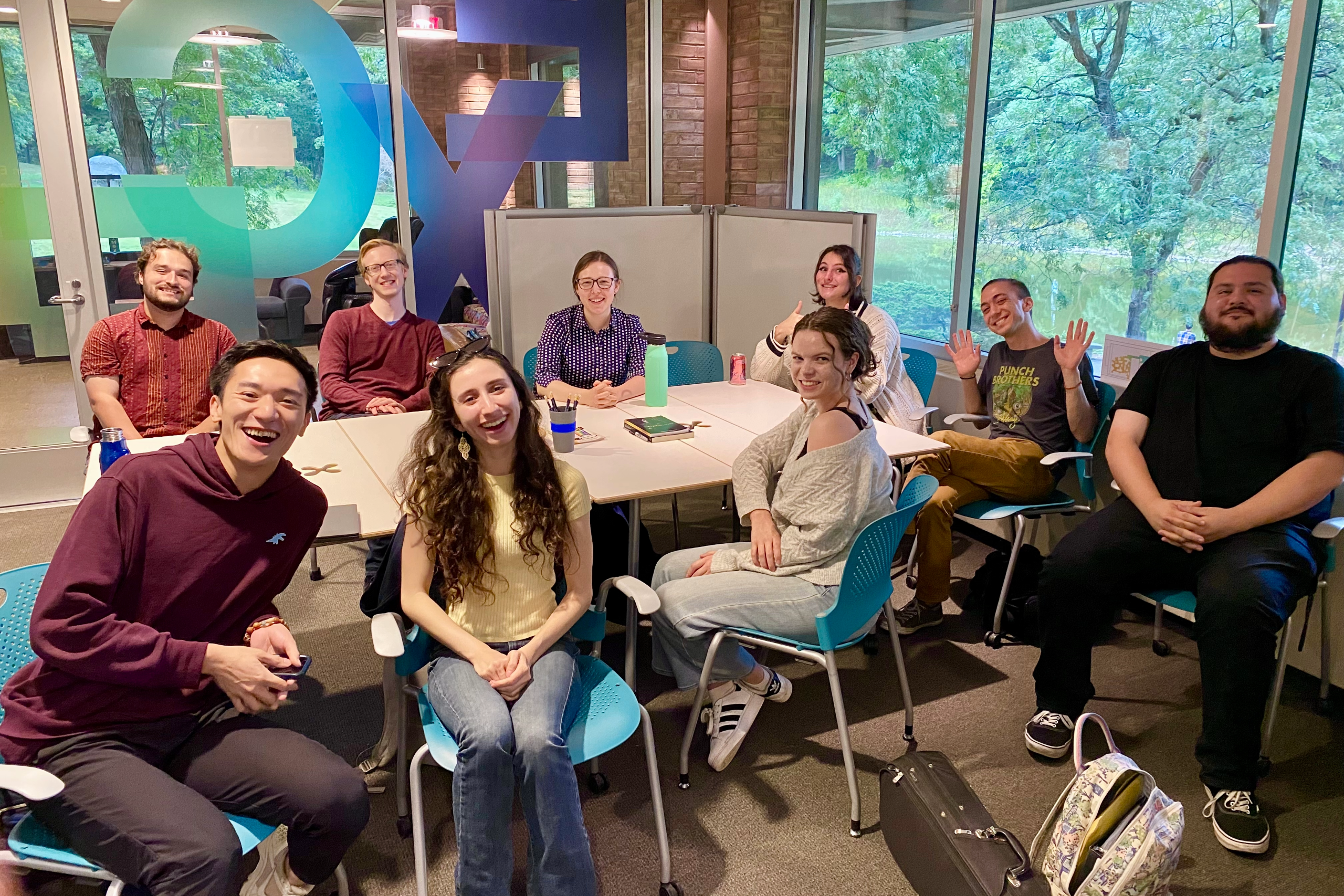 Students gathered in the EXCEL Lab around a conference table. In the background is a screen with the title "Student Producer Roundtable"