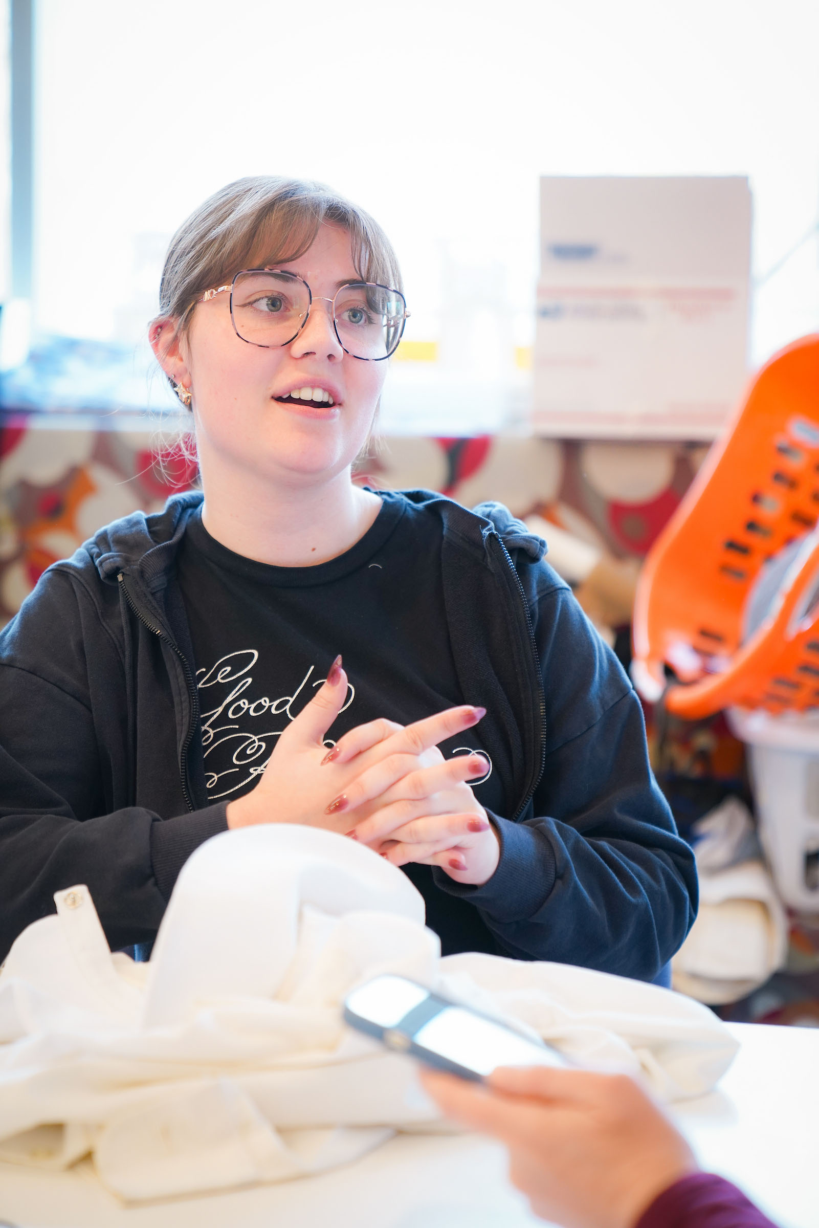 3 Ellie Van Engen studies costume design Costume Shop Candid photo of Ellie Van Engen, seated at a work table with a pile of cloth.