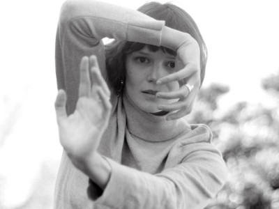 Black and white headshot of Alice Klock, with her arms in an abstract pose in front of her face