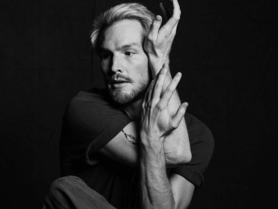 Black and white headshot of Florian Lochner, with this arms held in an abstract pose on the side of his face