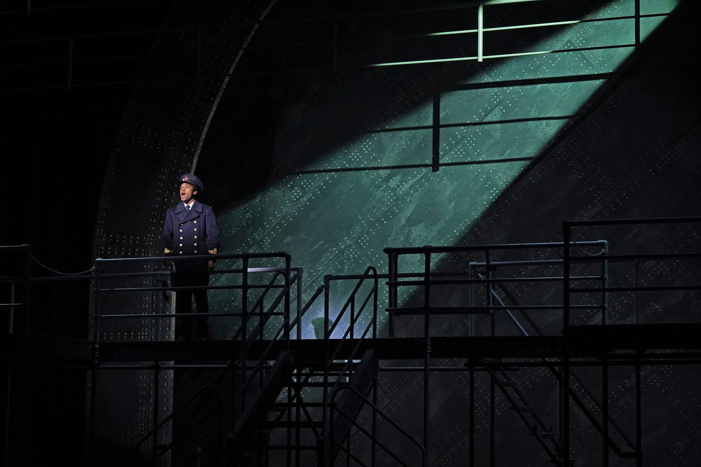 2b Keyon Pickett as William Murdoch Titanic scenery Keyon Pickett performs on stage as Titanic's William Murdoch, with a dramatic spotlight on the steel sides and rivets of his ship in the background scenery.