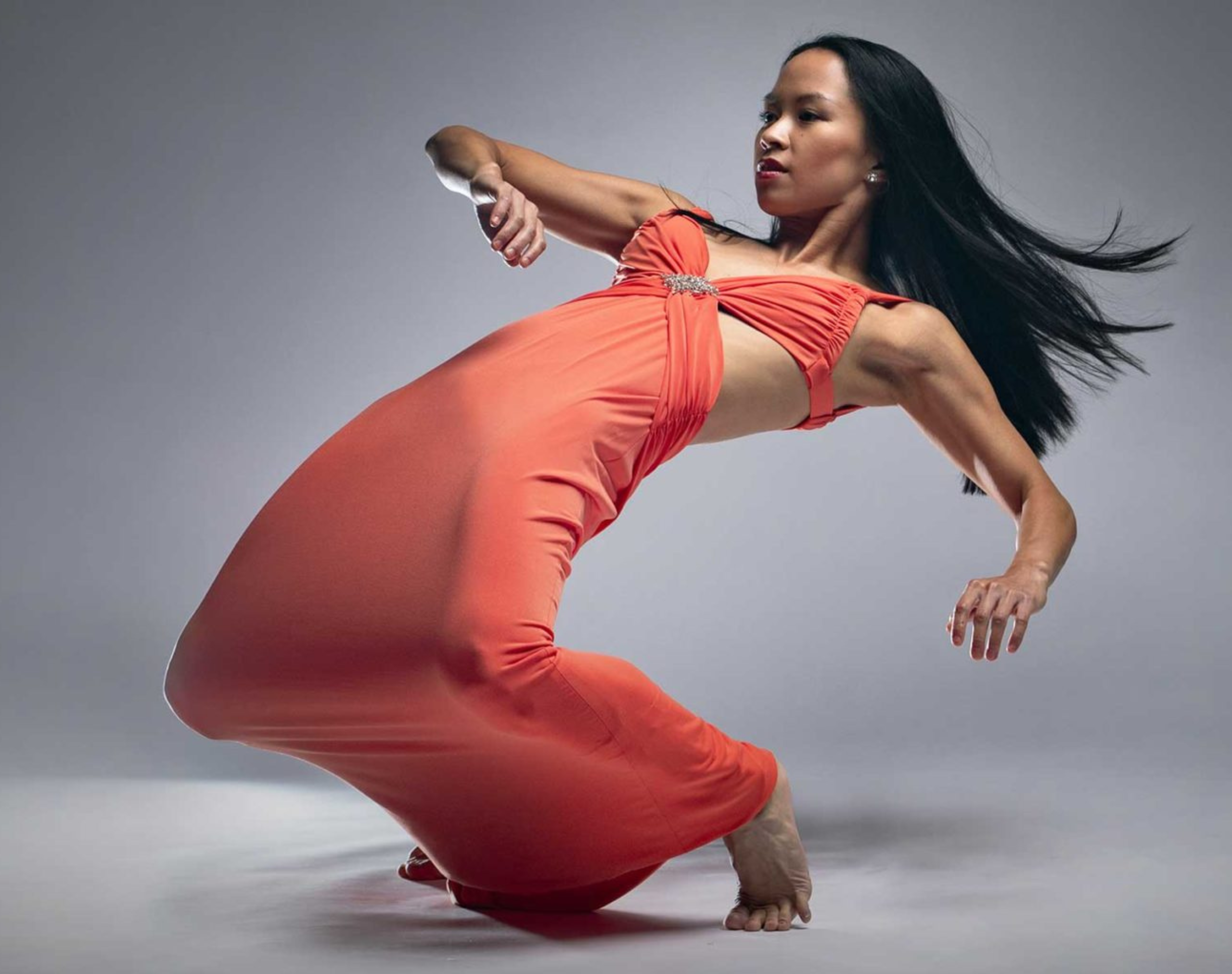 Photo of a dancer holding a dynamic pose wearing an orange dress 