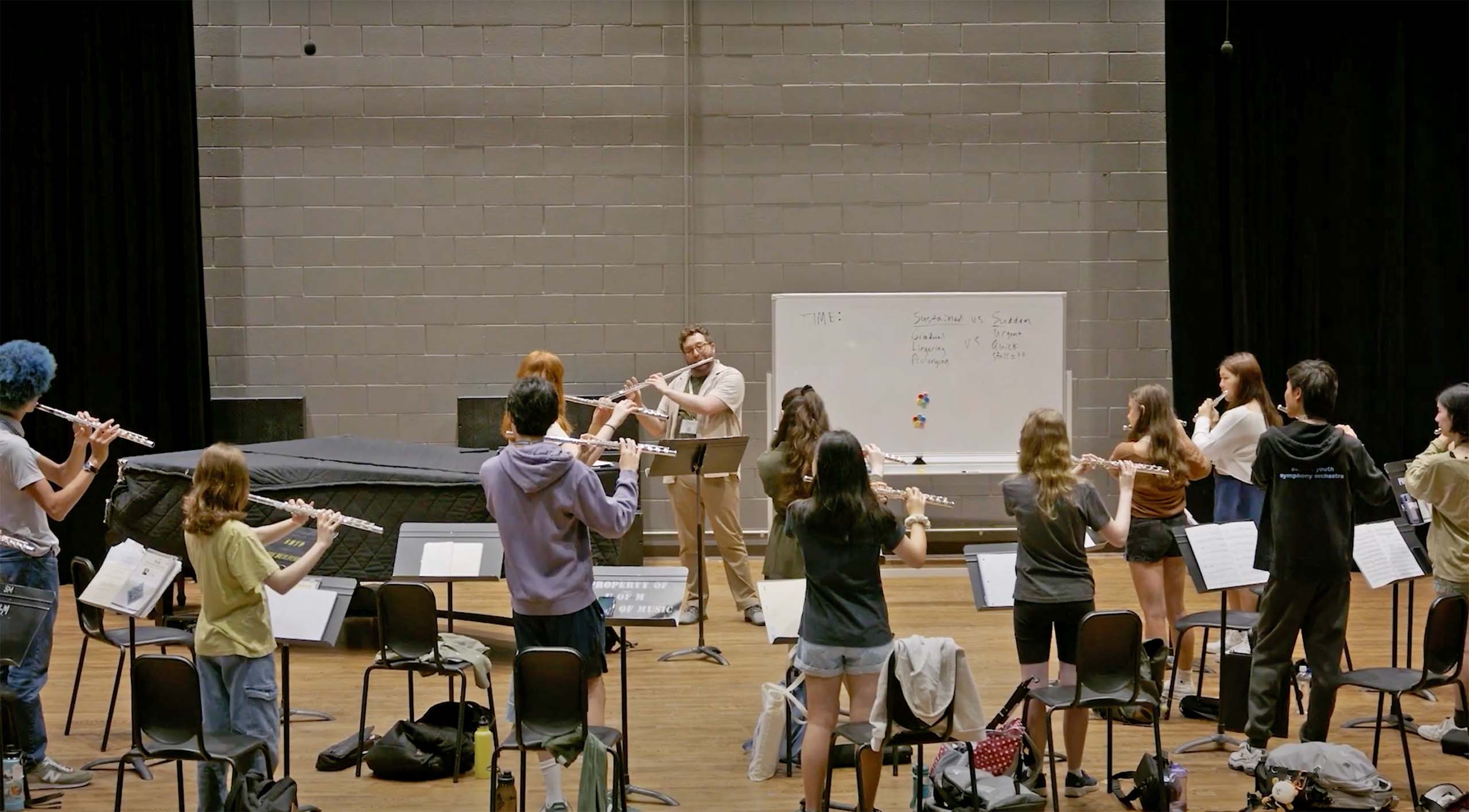 A group of MPulse youth flute players rehearse standing up with a conductor.