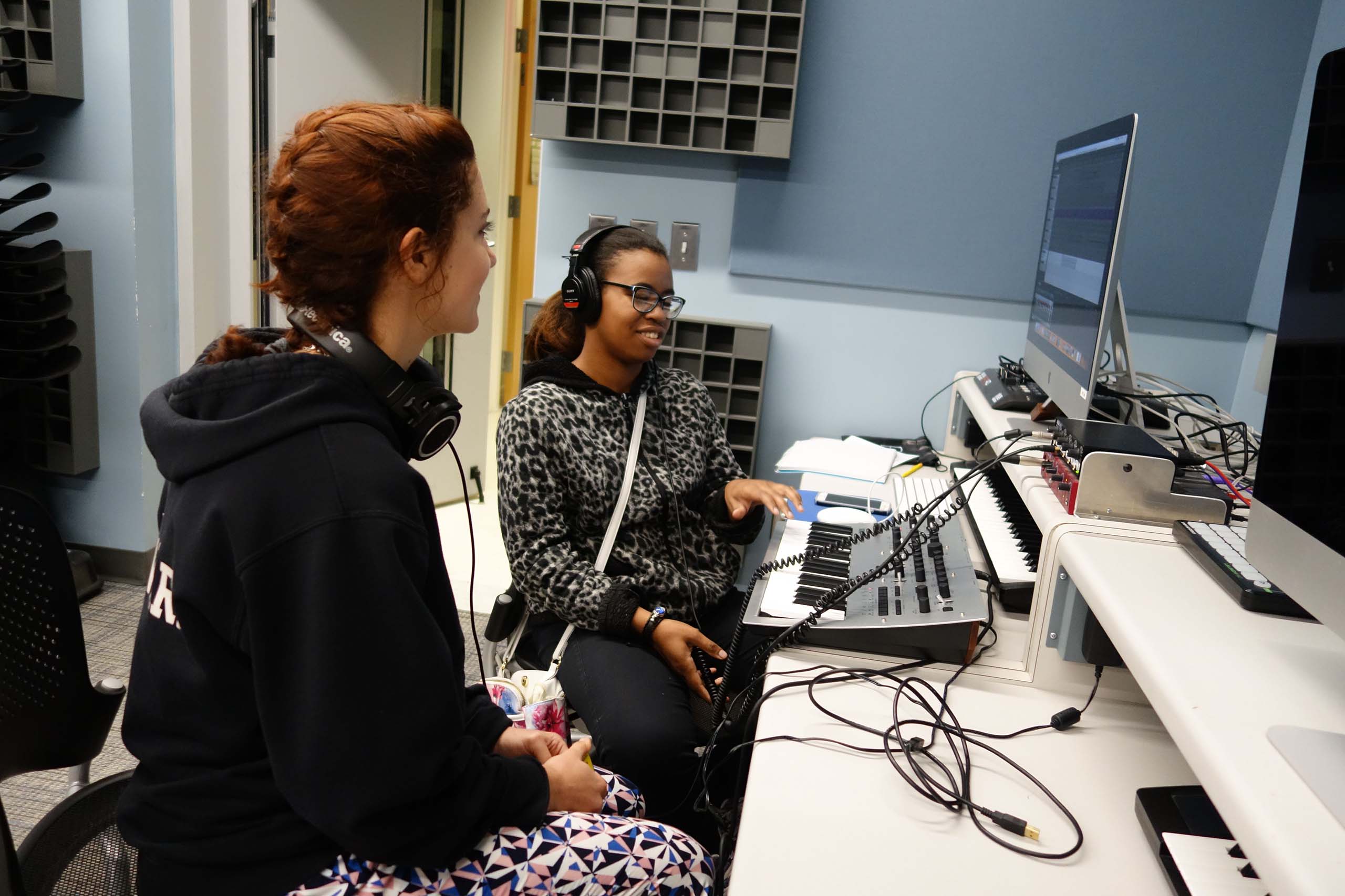 Two MPulse students work together seated at a computer with a connected keyboard; both wearing headphones.