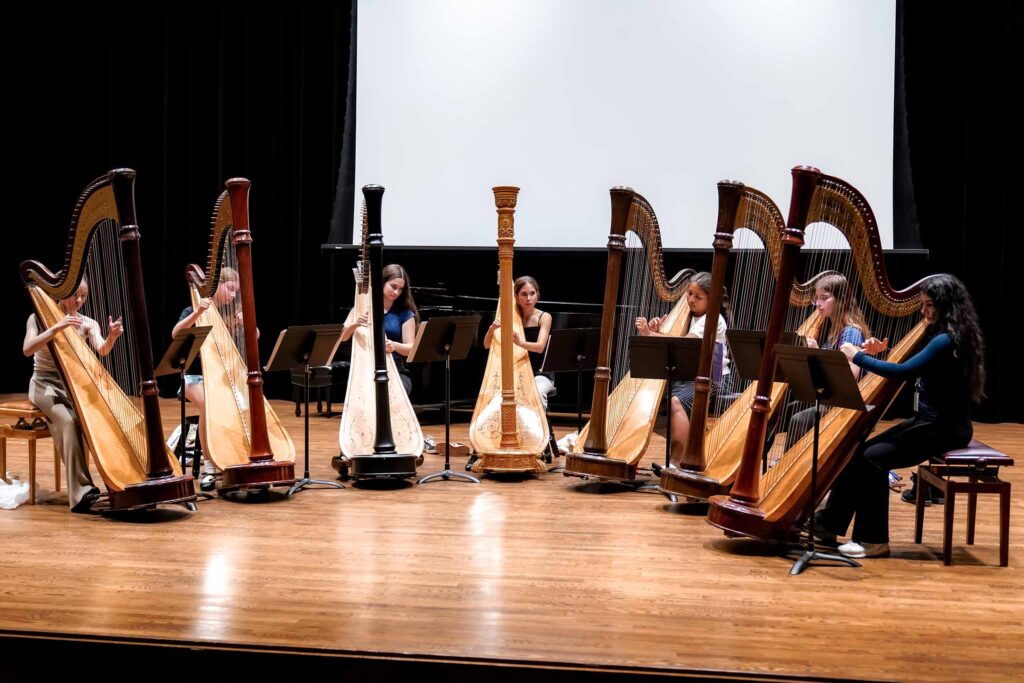 Seven MPulse students all play harps in a row on a stage.