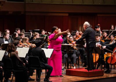 A vocal soloist is performing in front of the USO in a pink dress and reaches out her hand to the audience