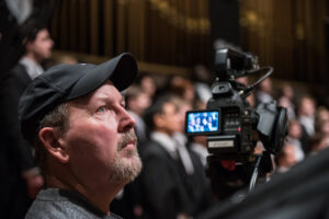 Bob Berg focuses on camera work as the Men's Glee Club performs in the background.