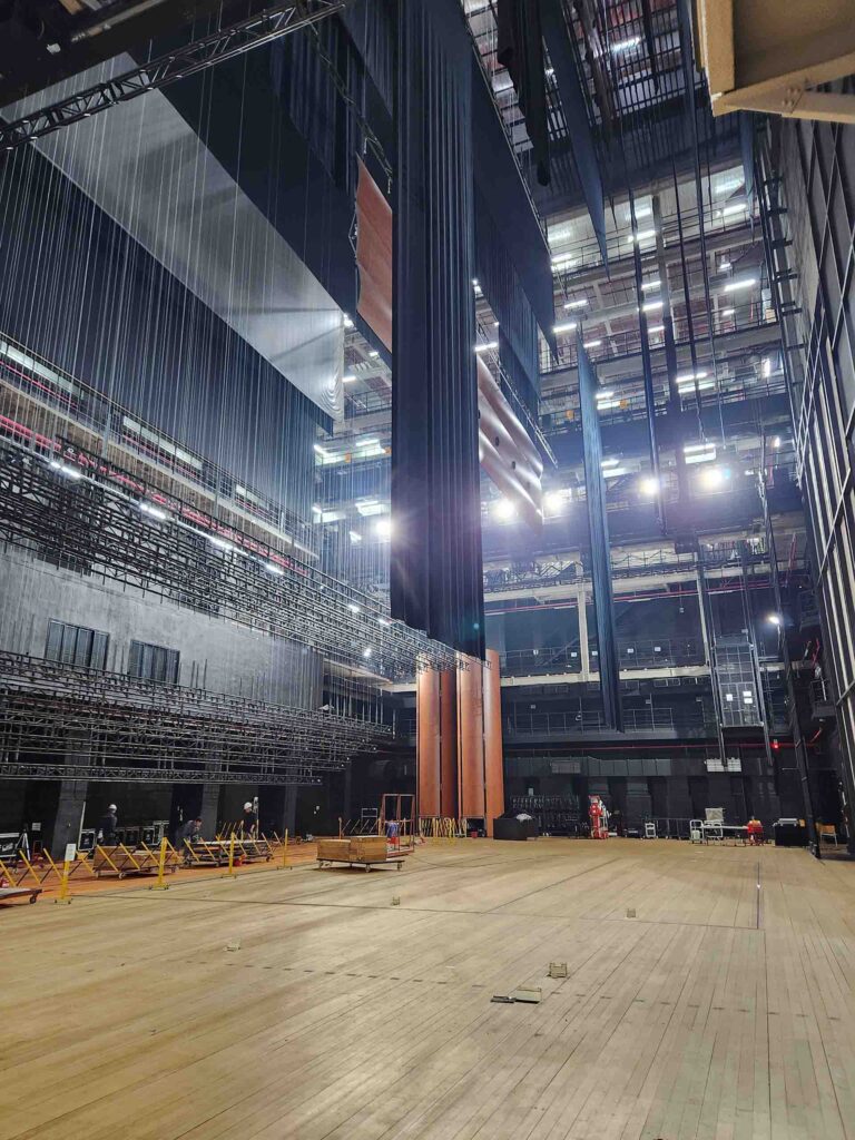 A side-view of a stage, showing its expansive six-story adjacent backstage areas, with hanging black curtains and lighting structures.