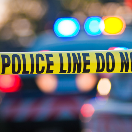 Yellow Police Line tape, with police vehicle flashing lights in the background.