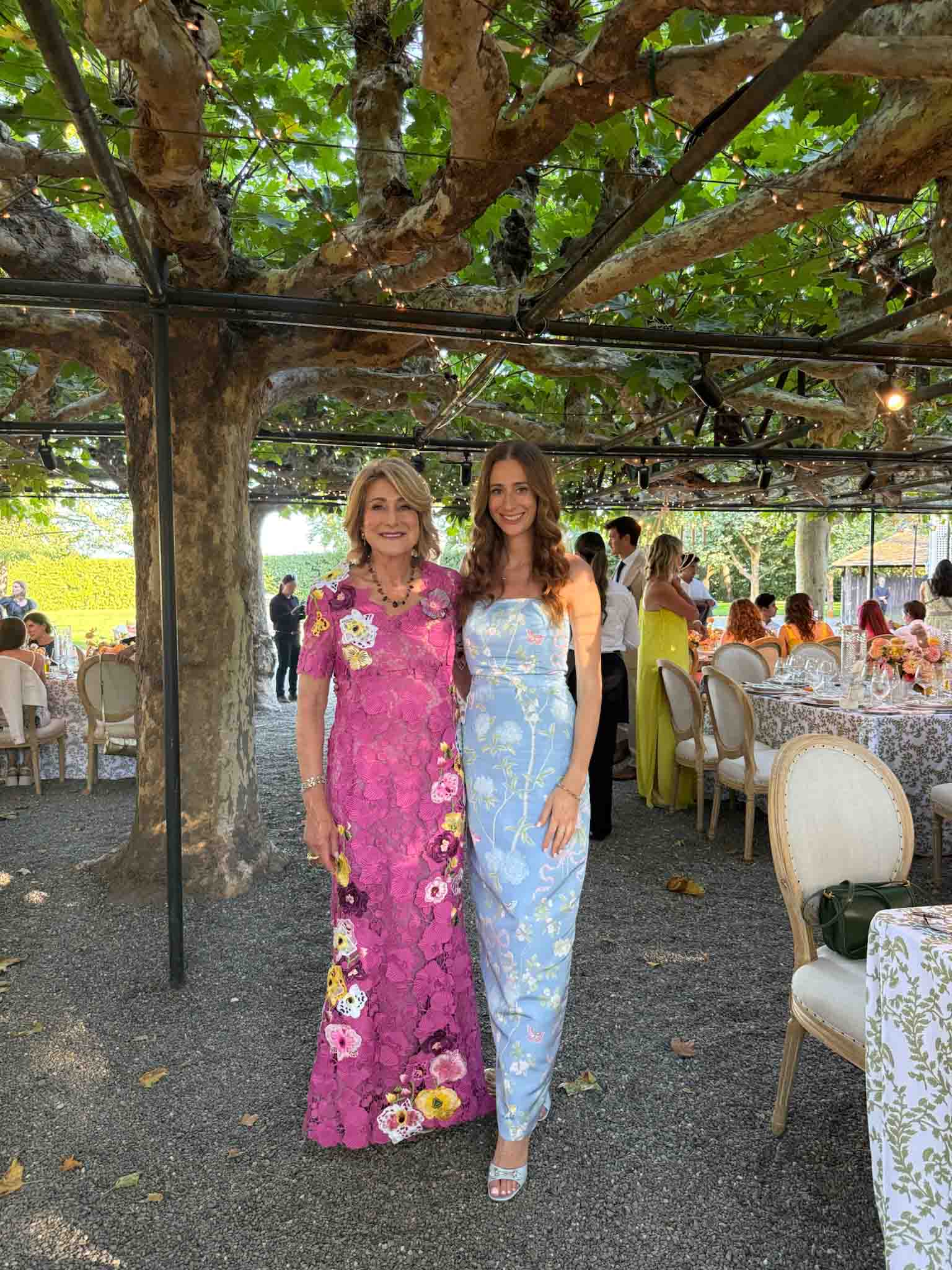 Alyssa Taubman and Talia Rothman pose standing in formal dresses at an outdoor reception.
