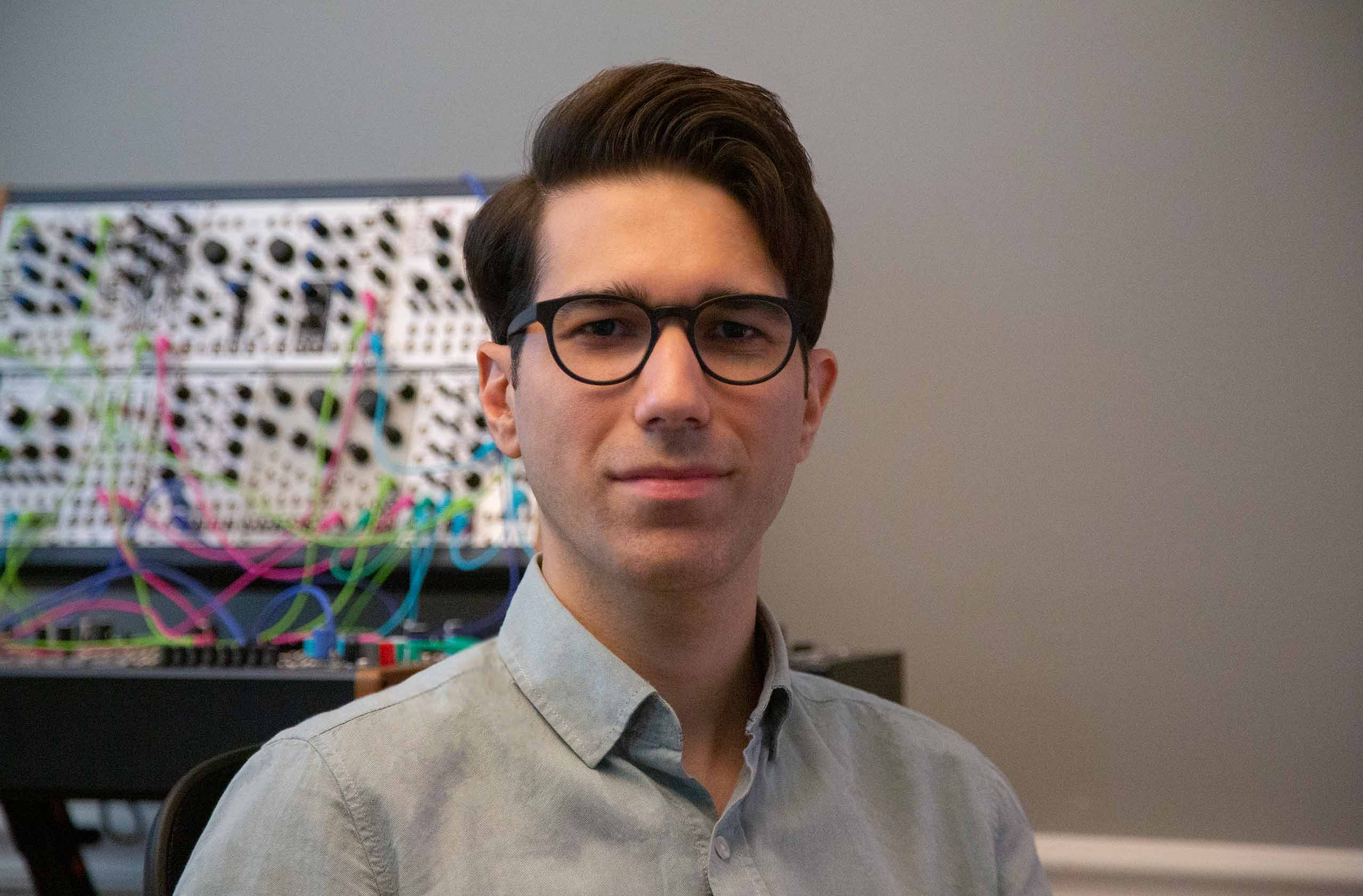 Headshot of Anıl Çamcı with electronic equipment in the background.