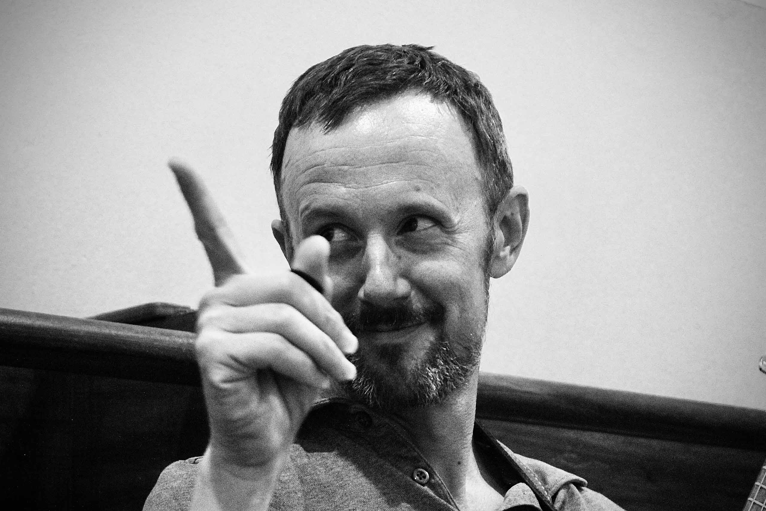 Greyscale candid photo of Bret Hoag, gesturing with one pointed finger.