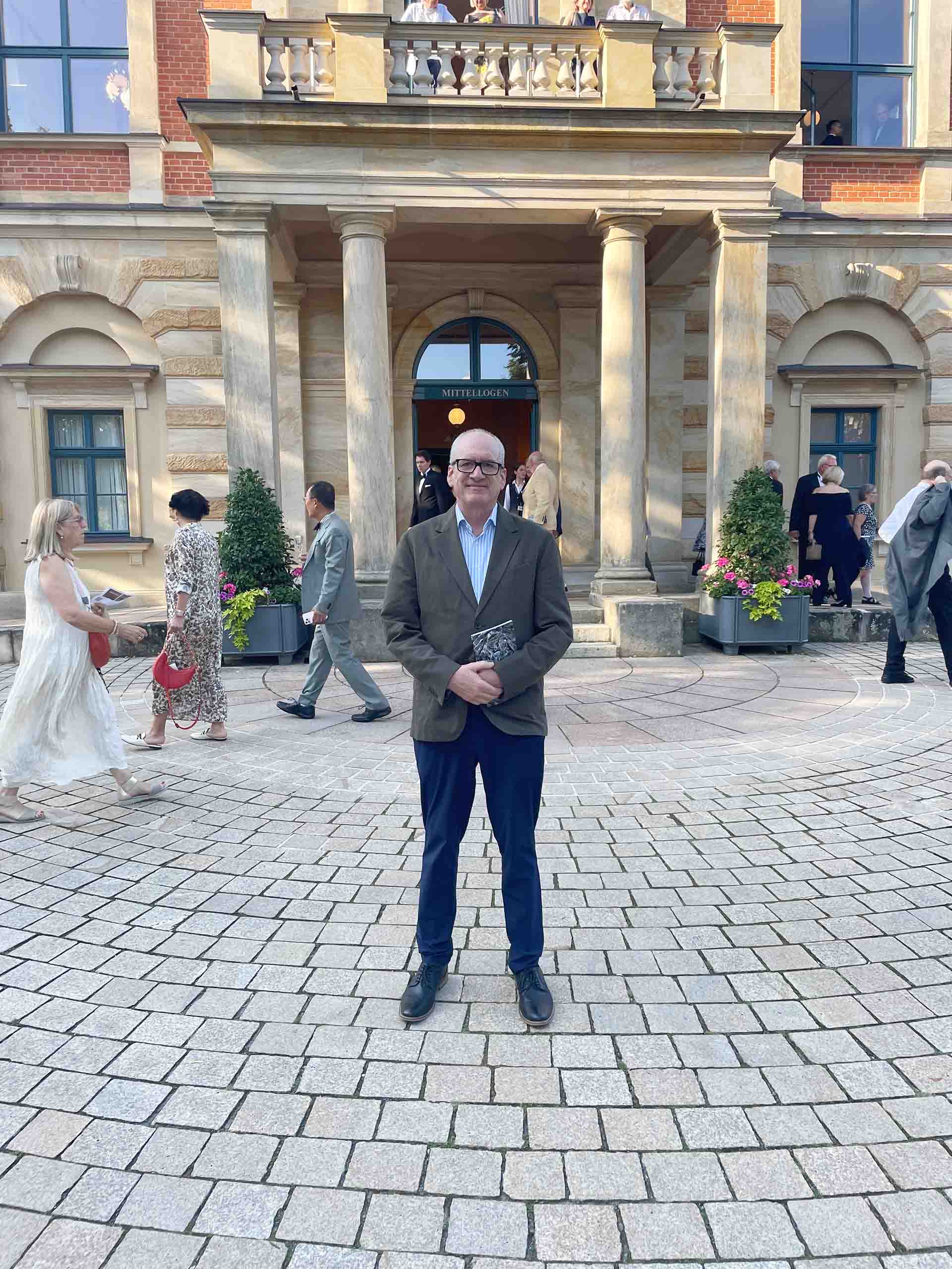 Brian Moll poses standing outdoors in a brick-paved courtyard in front of a classical style building.