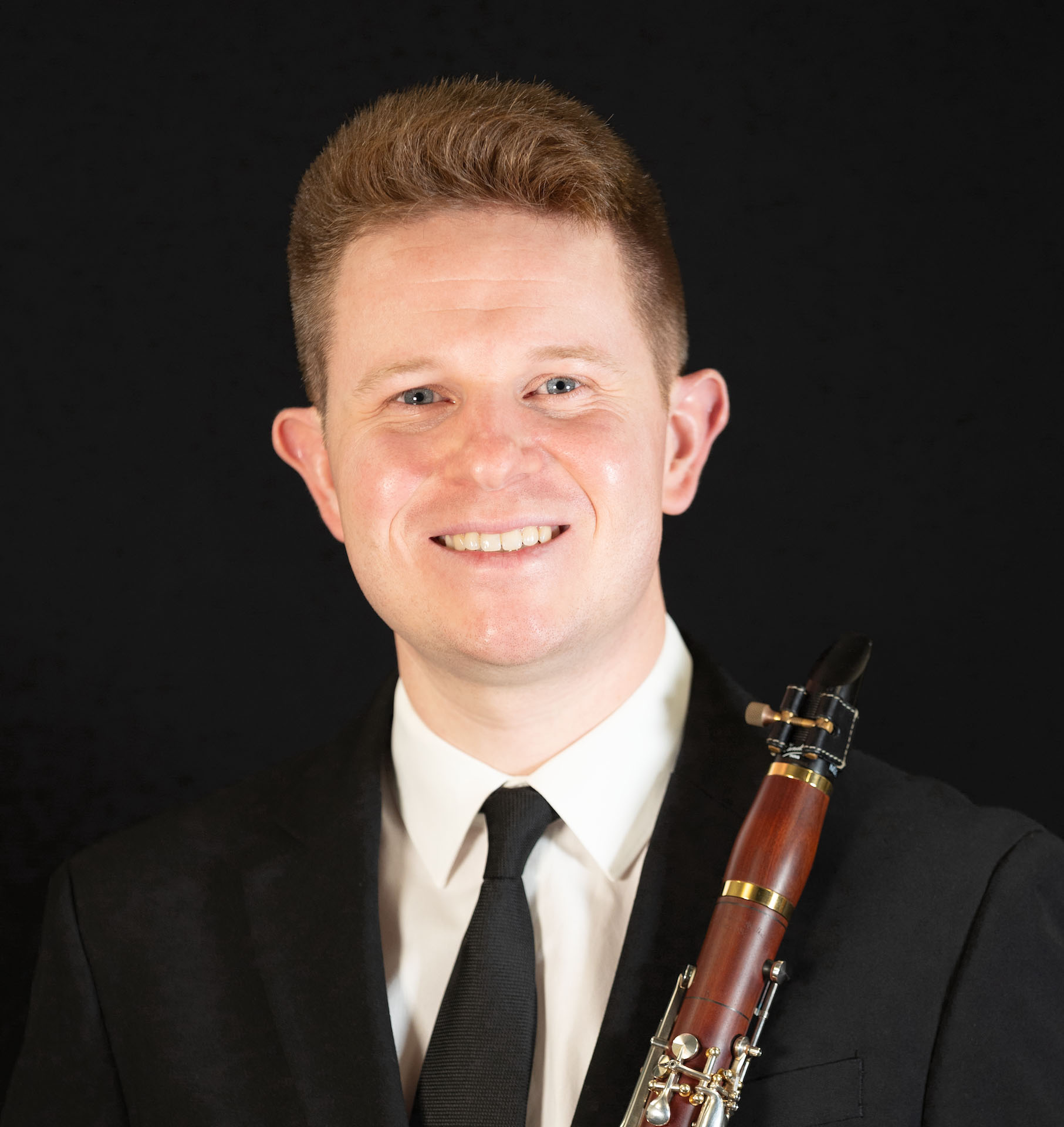 Studio portrait of Chadwick Thomas holding a brown wooden clarinet.