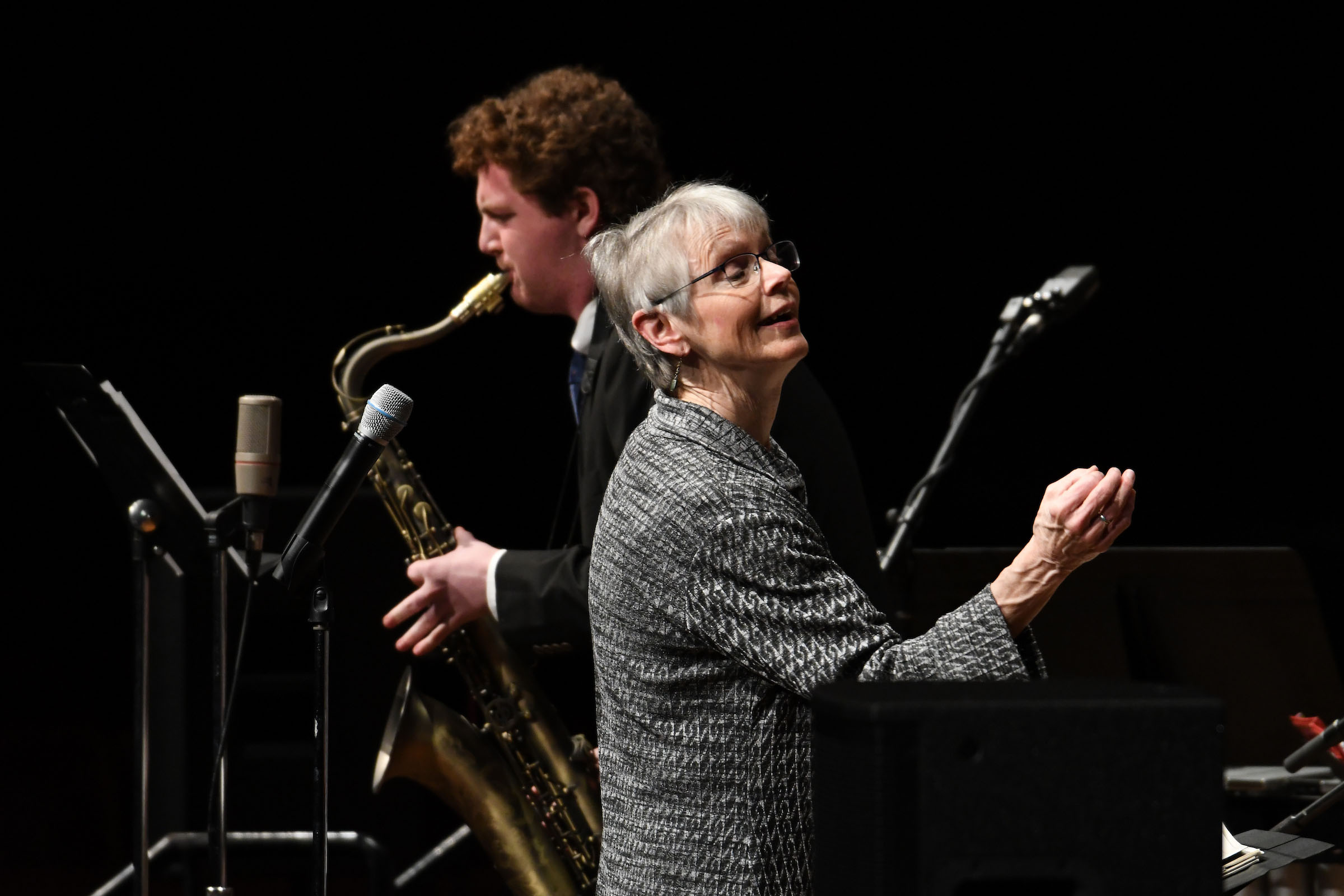 Ellen Rowe conducts a jazz performance, as a saxophone soloist stands playing behind her.