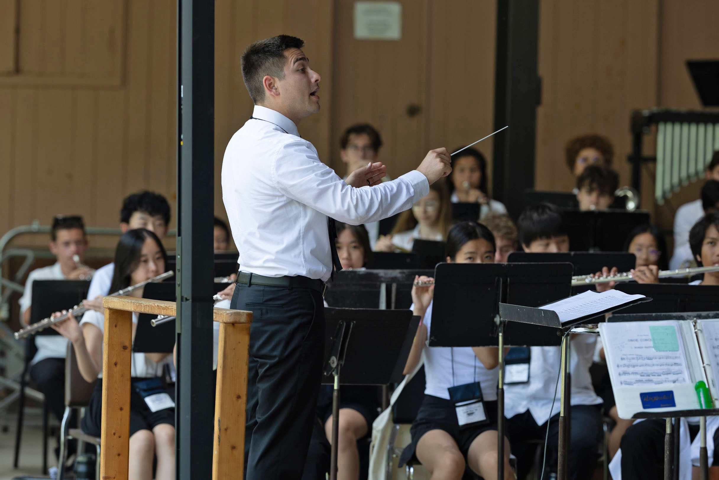 Elliot Polot conducts a band featuring young students in performance; with all wearing black and white concert attire.