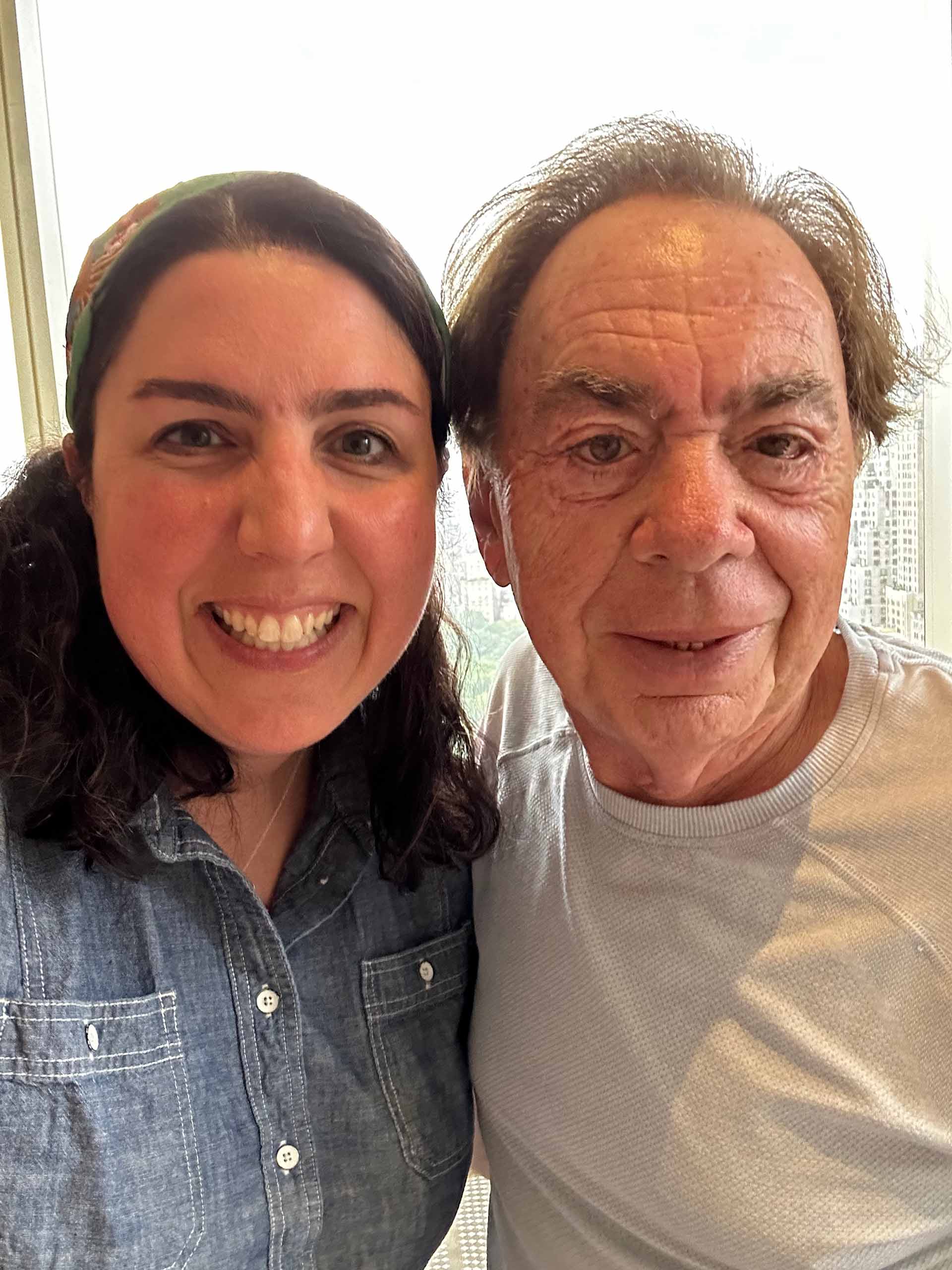 Erin Craig and Andrew Lloyd Webber casually pose together next to a large window.