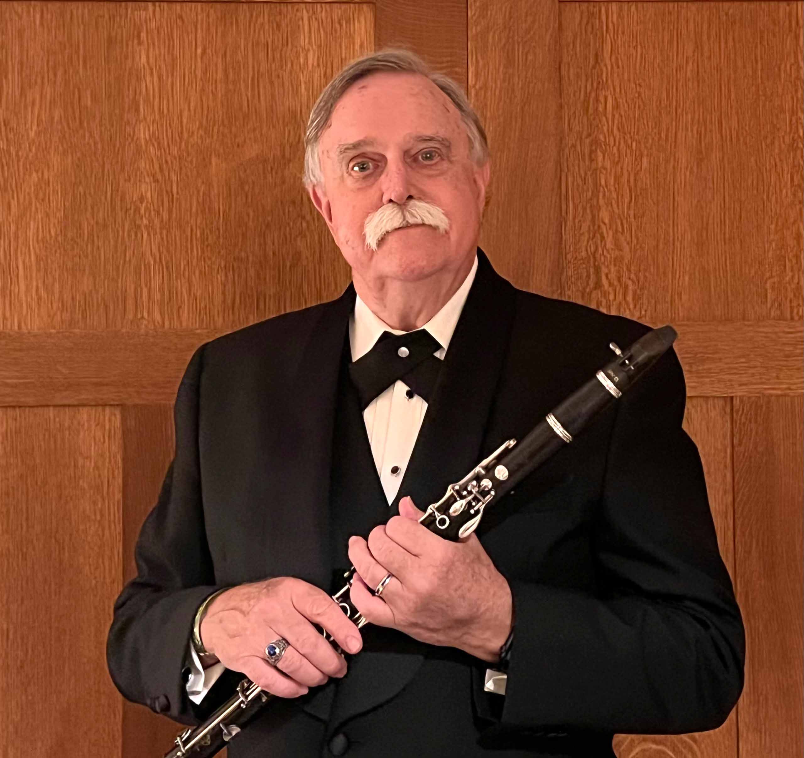 Greg Heuer stands holding his clarinet in concert attire.