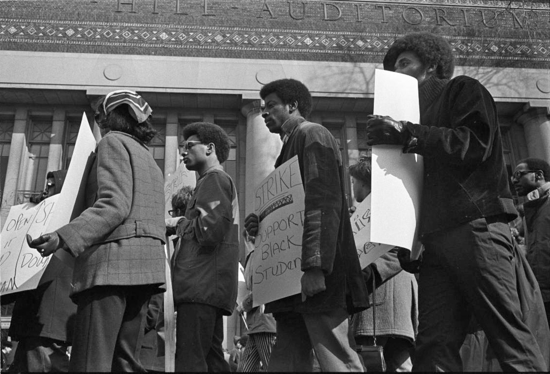 A mid-to-late 20th century scene of protesters carrying signs outside Hill Auditorium.