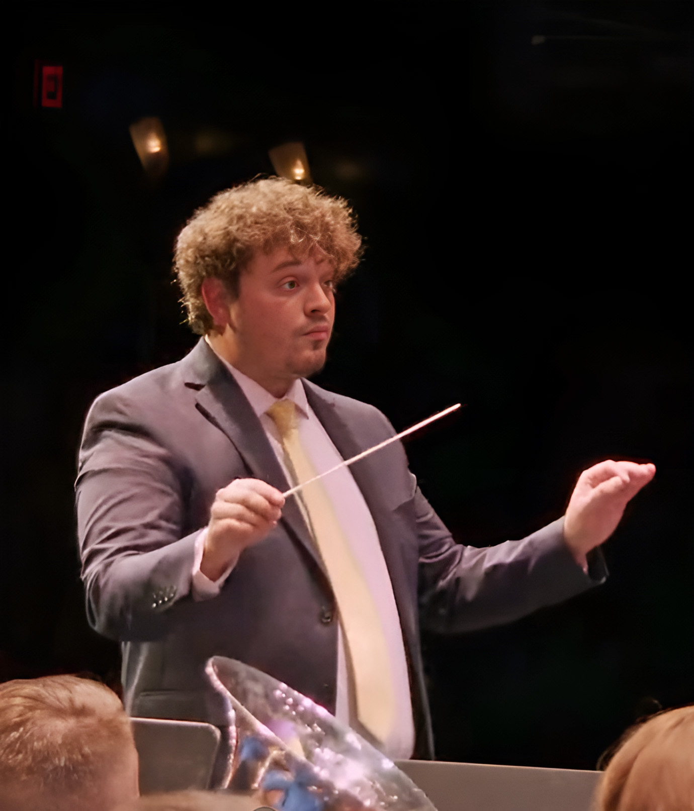 James A. Long conducts in a dark concert hall during a band performance, attired in a suit and tie.