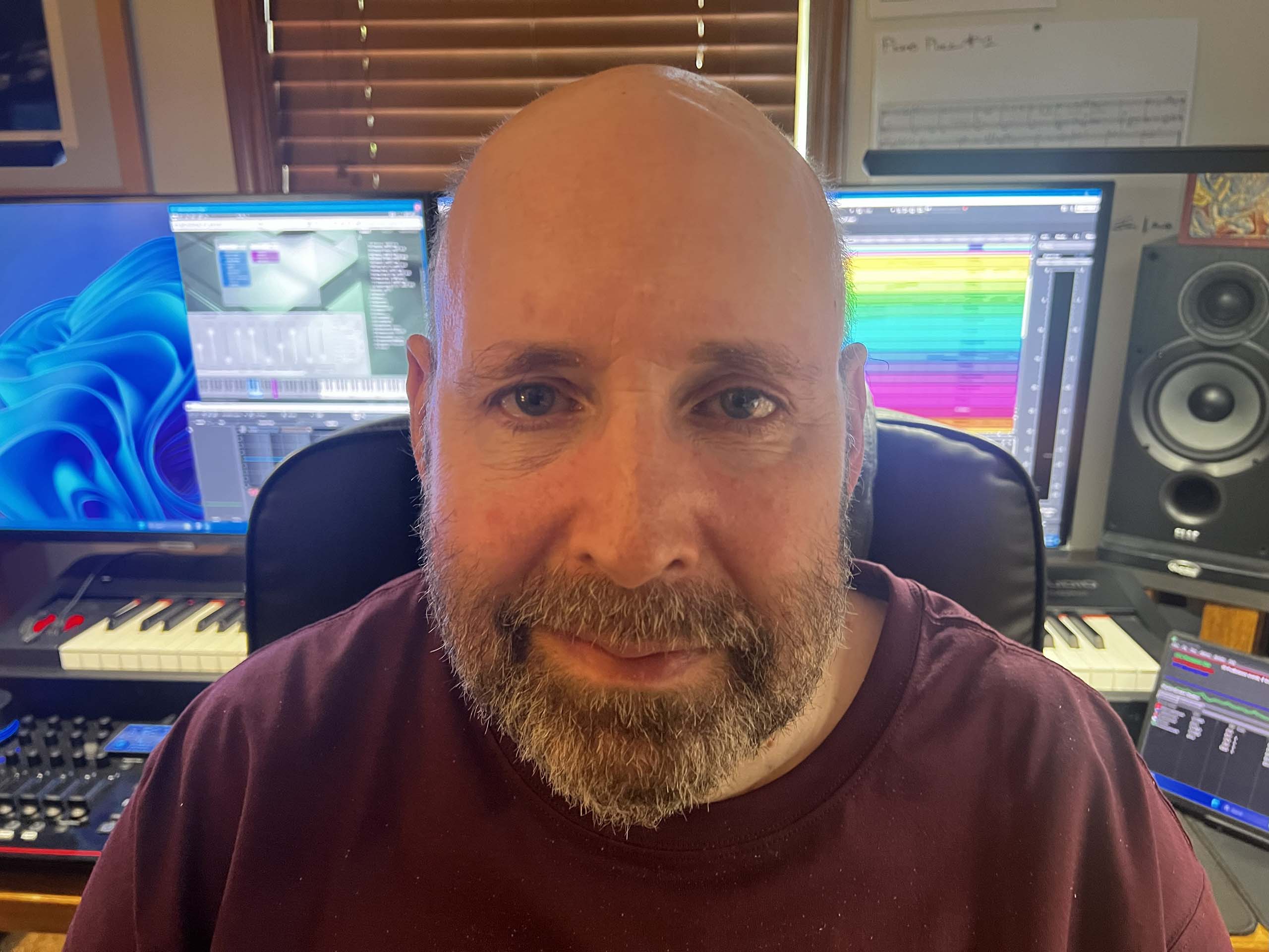 Headshot of James Johnston seated at a workstation with keyboard, mixer, and music software on computer screens.