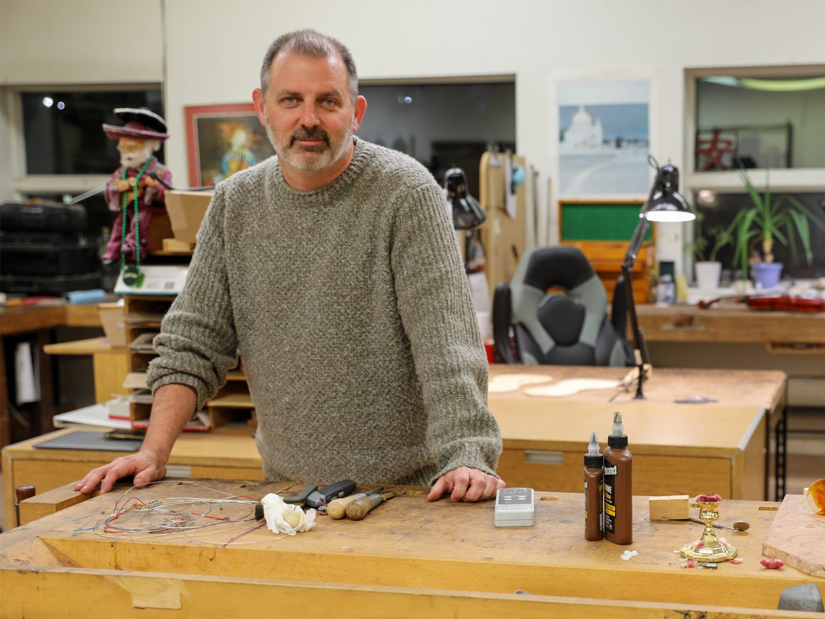 James Ryan Bodiford poses standing in a workshop space with tools, glue, and wax on the workbench in front of him.